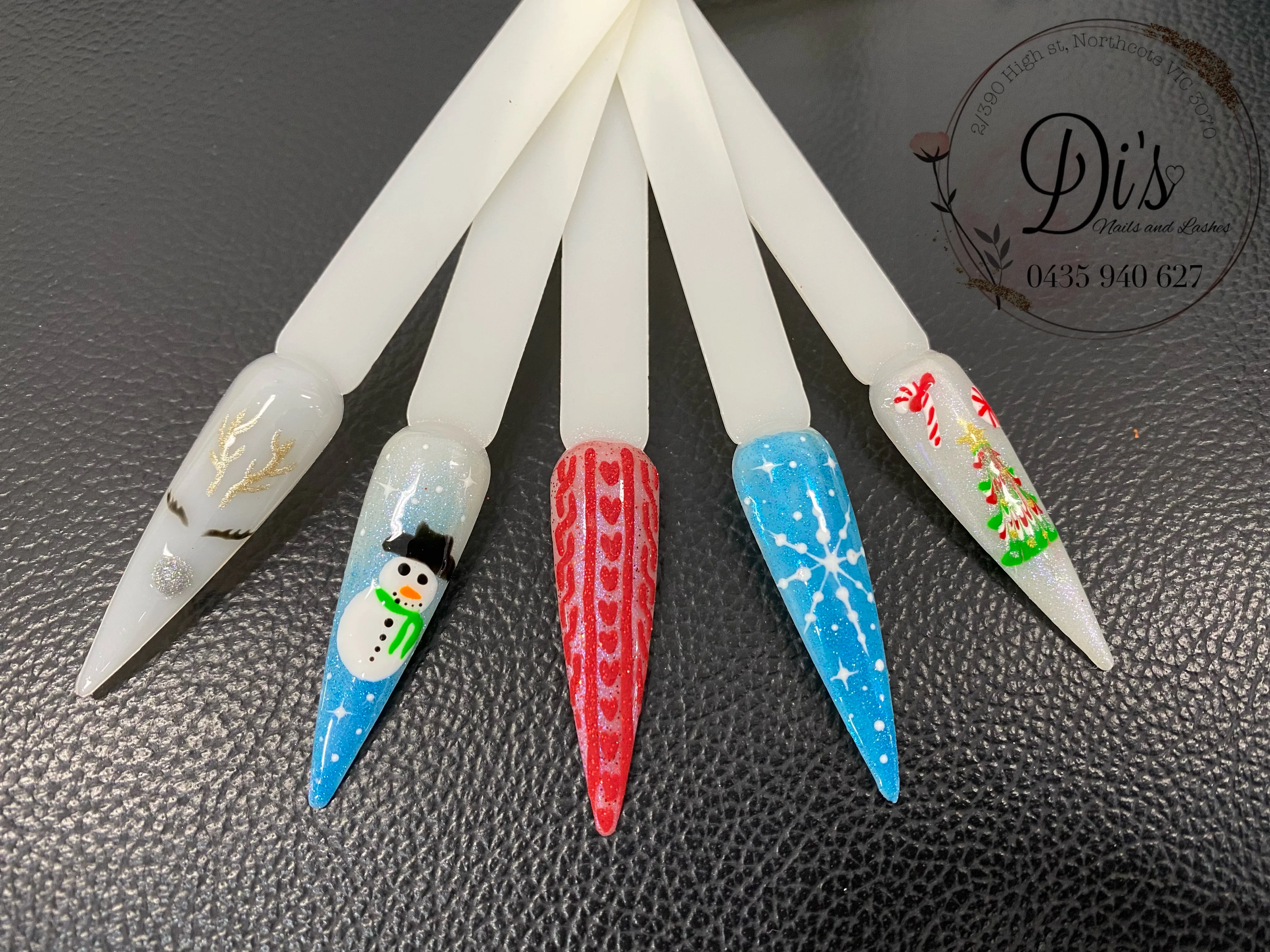 Christmas display nail tips with festive art — snowman, candy cane, tree, snowflake