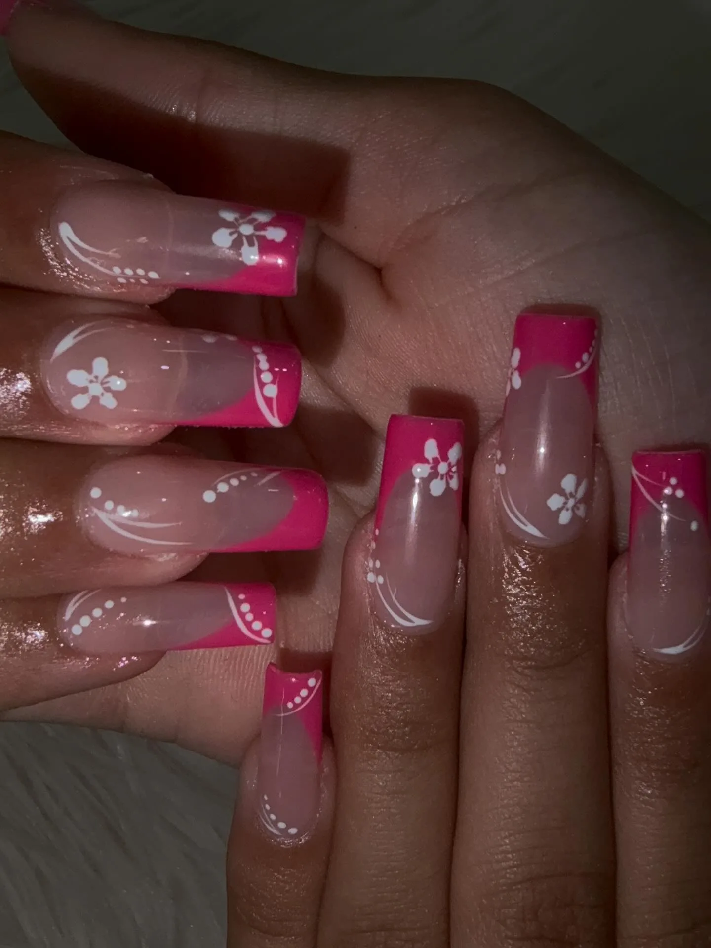Long square hot-pink French tips with white hand-painted hibiscus flowers, dots and swirl line art, glossy — on white fur