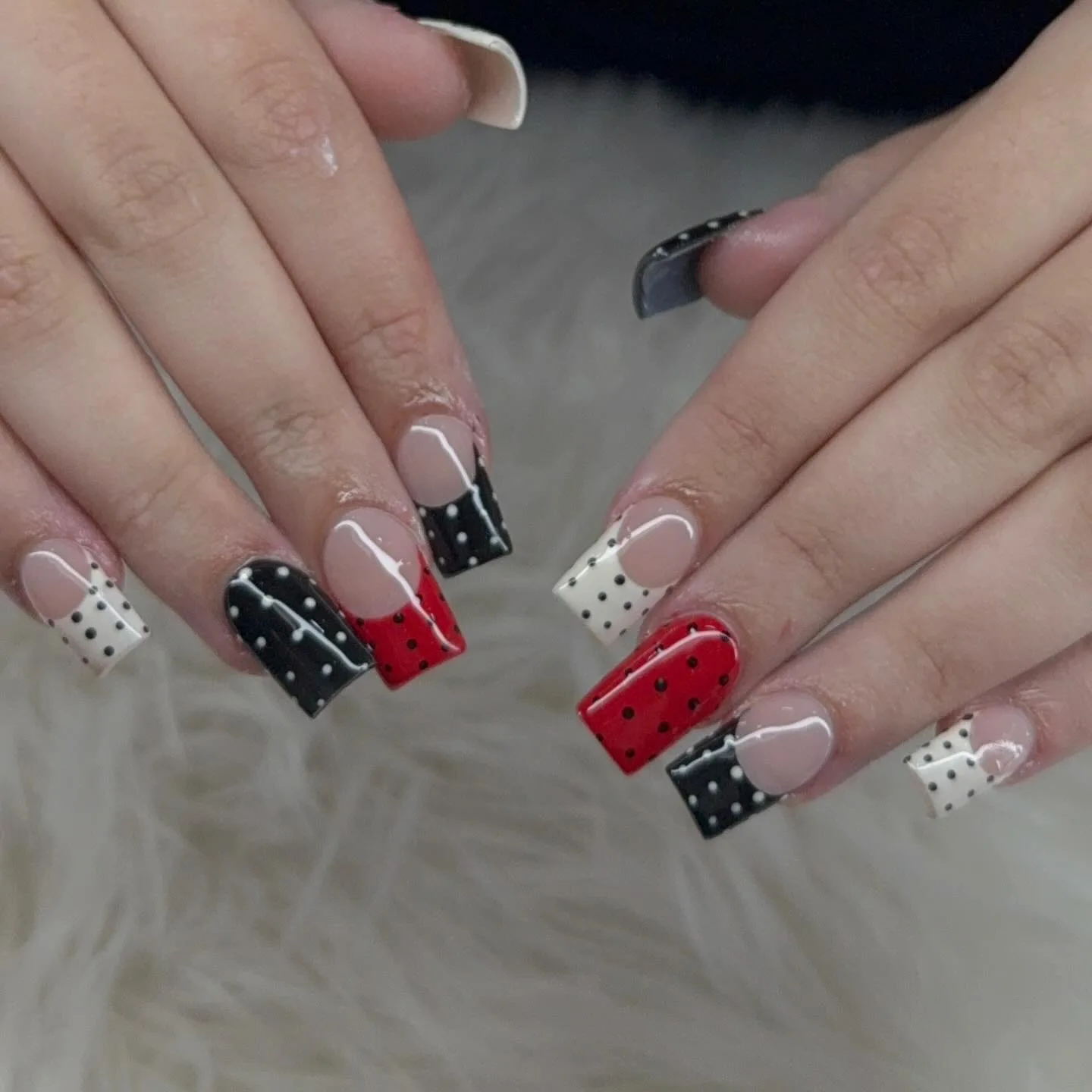 Square French tips in red, black and cream with black-and-white polka dots over pink nude, retro high-gloss styling — on white fur