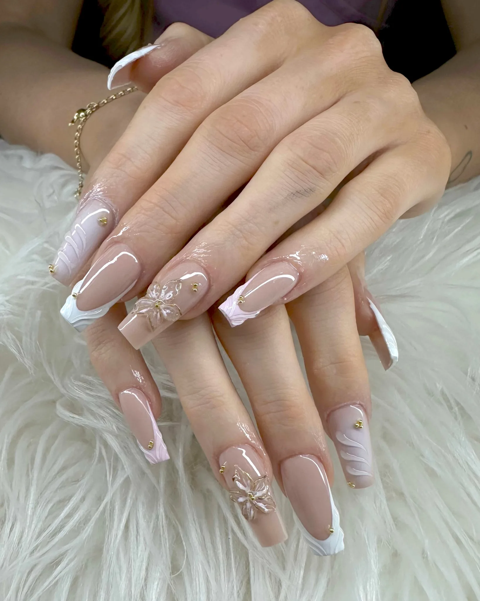 Long coffin bridal nails with sculpted pearlescent 3D florals, gold caviar bead accents and carved white swirl tips, fine gold chain bracelet — on white fur